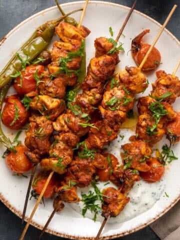 Chicken kebabs with roasted green peppers and tomatoes on a white plate.