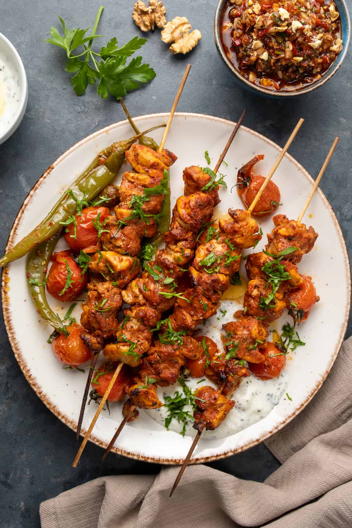 Chicken skewers on a white plate and ezme salad on the side.