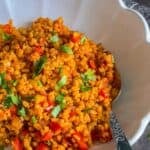 A close-up of Turkish bulgur pilaf with red peppers and parsley in a white bowl with a spoon, labeled “Bulgur Pilavi” and “giverecipe.com.”