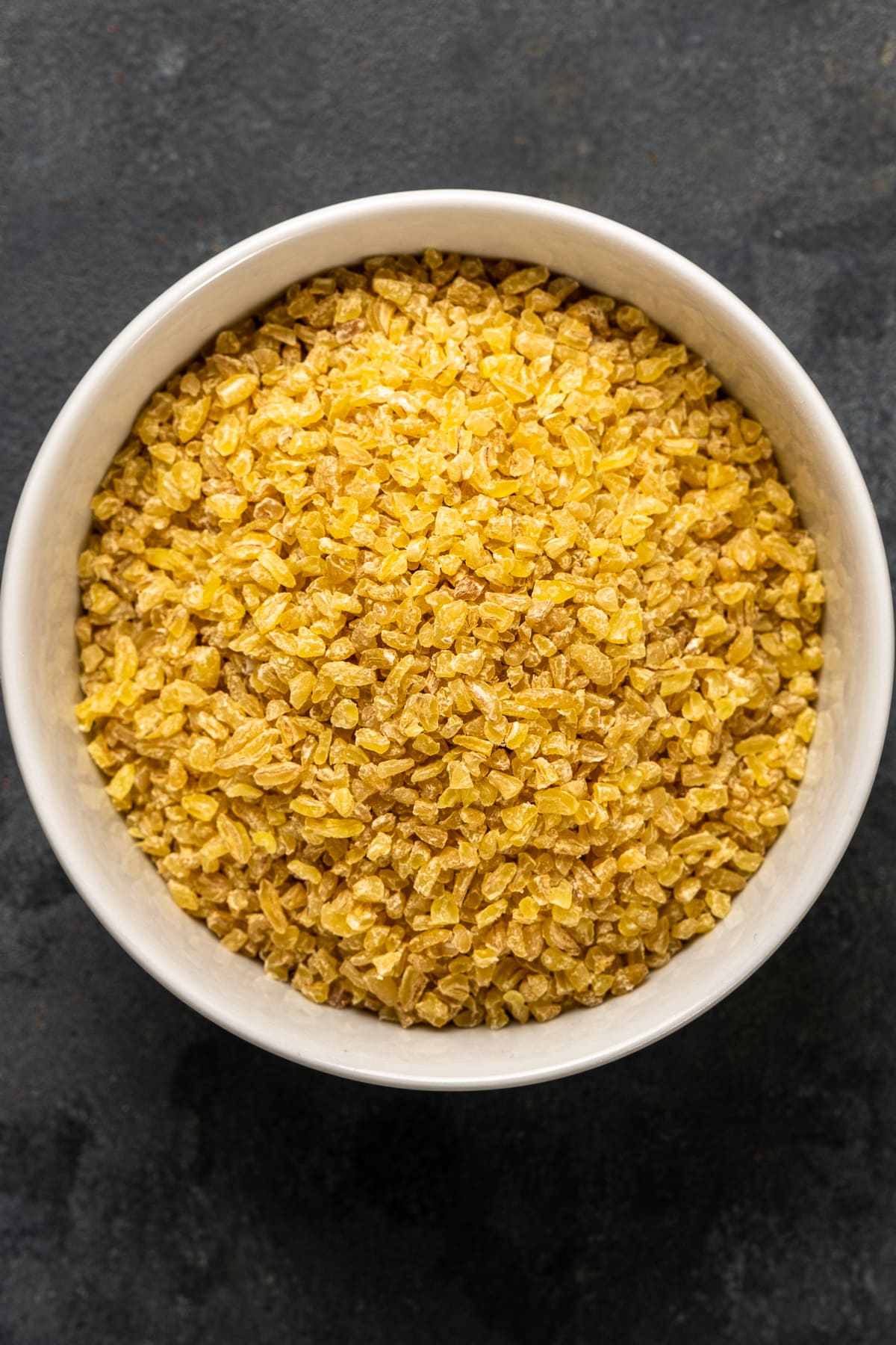 Coarse bulgur in a white bowl on a dark background.