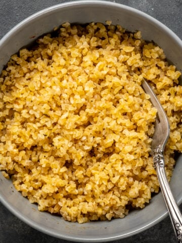 Medium bulgur after soaked in a grey bowl with a fork inside it.