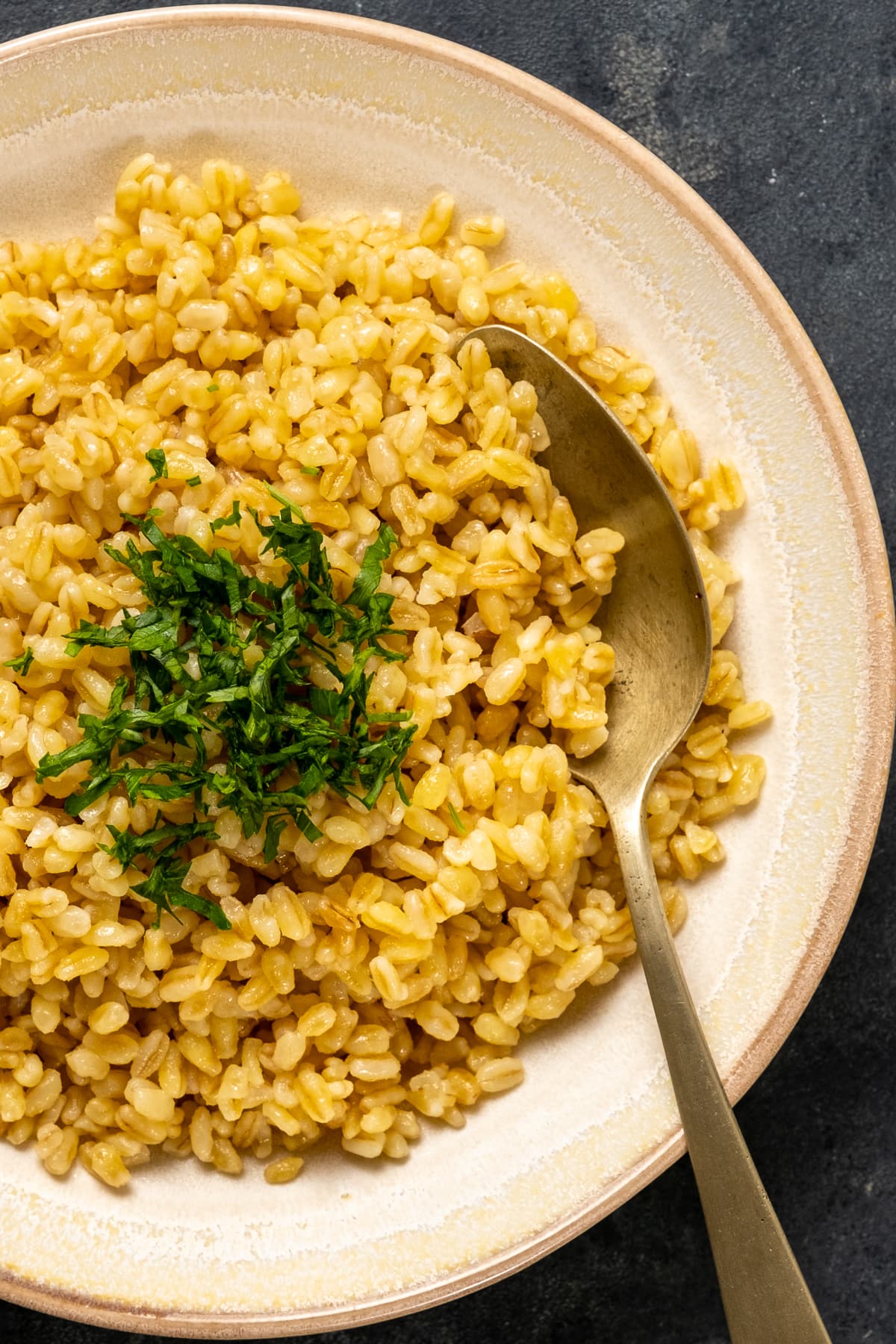 Cooked very coarse bulgur topped with chopped parsley in a white bowl with a spoon inside it.