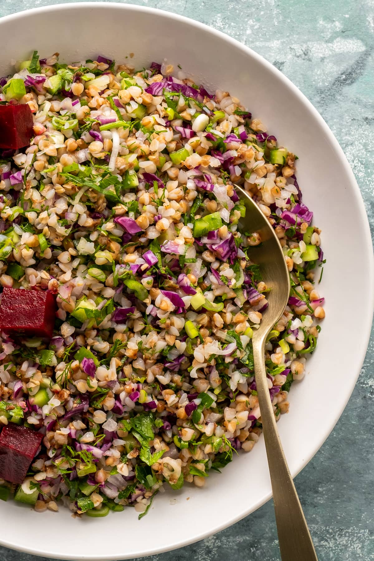 Buckwheat salad with red onions, red cabbage and herbs topped with pickled beets in a white bowl and a spoon in it.