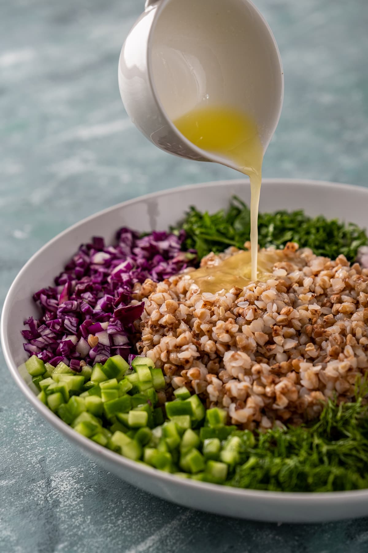 Pouring lemon dressing in a white sauce bowl over the buckwheat salad.