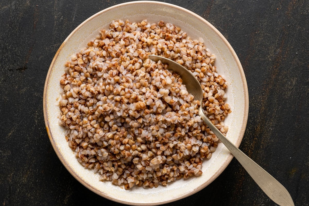 Cooked toasted buckwheat in a white bowl and a spoon inside it.