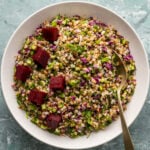 Buckwheat salad topped with pickled beets in a white bowl with a spoon in it.