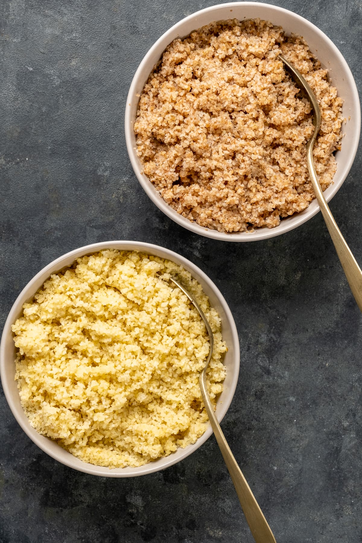 Soaked red and white fine bulgur in two white bowls with spoons inside them.