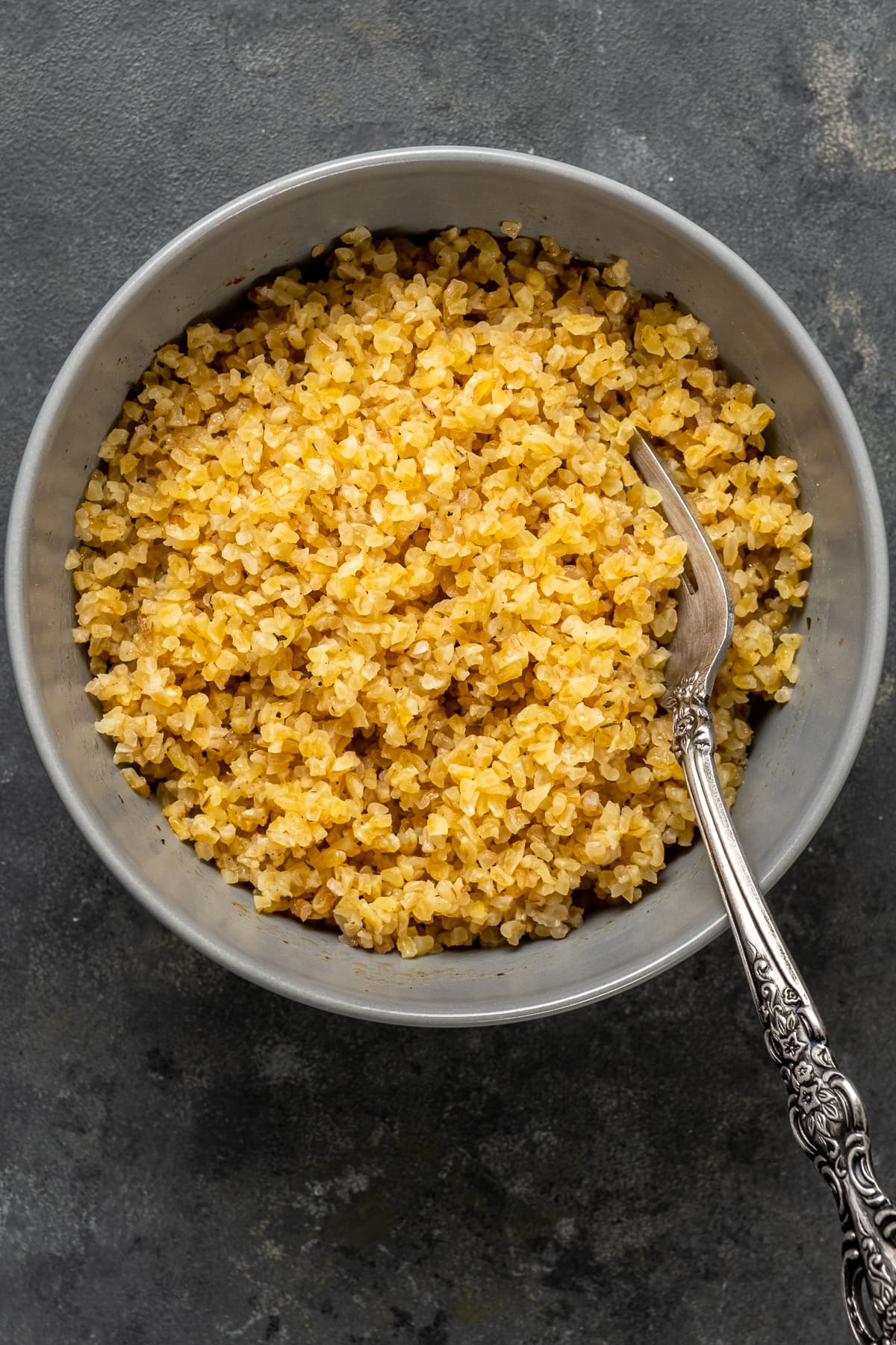 Medium bulgur in a grey bowl after soaking with a fork inside it.