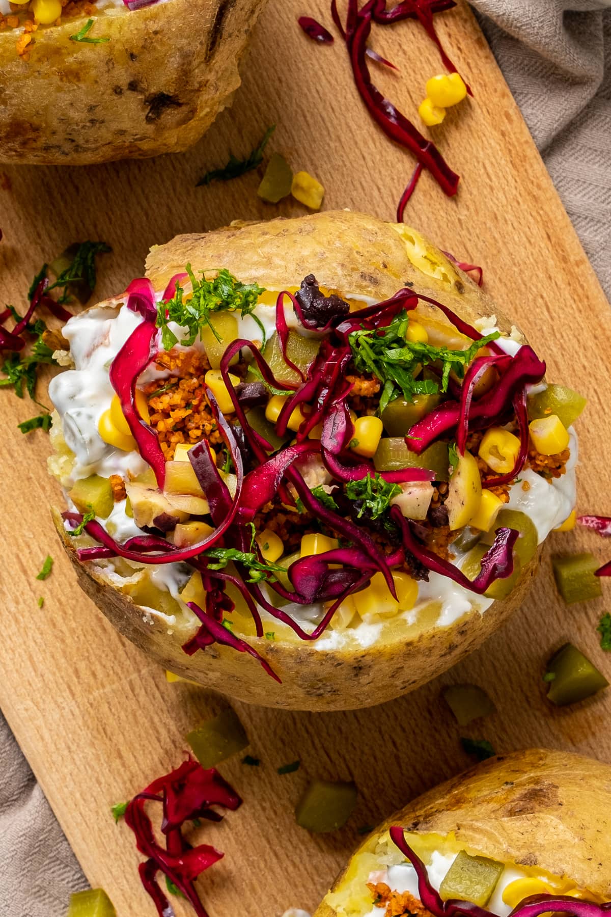 Kumpir loaded with bulgur salad kisir, corn, olives, dill pickles and red cabbage on a wooden board.