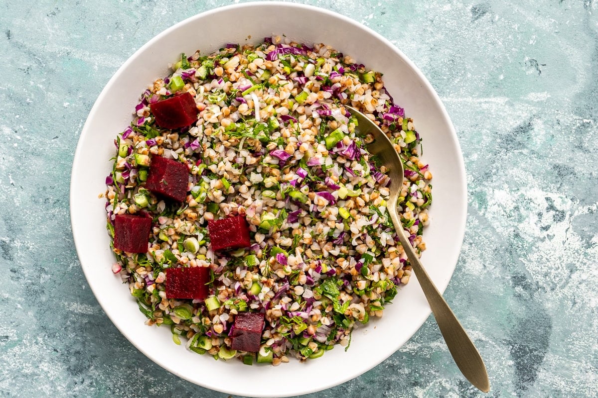 Buckwheat salad with veggies in a white bowl with a spoon in it.