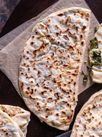 Homemade Turkish spinach and cheese gozleme with golden brown spots, served whole and sliced on a wooden board.