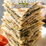 Spinach and cheese filled gozleme served in a stack on a white plate and a half of a cherry tomato on the side.