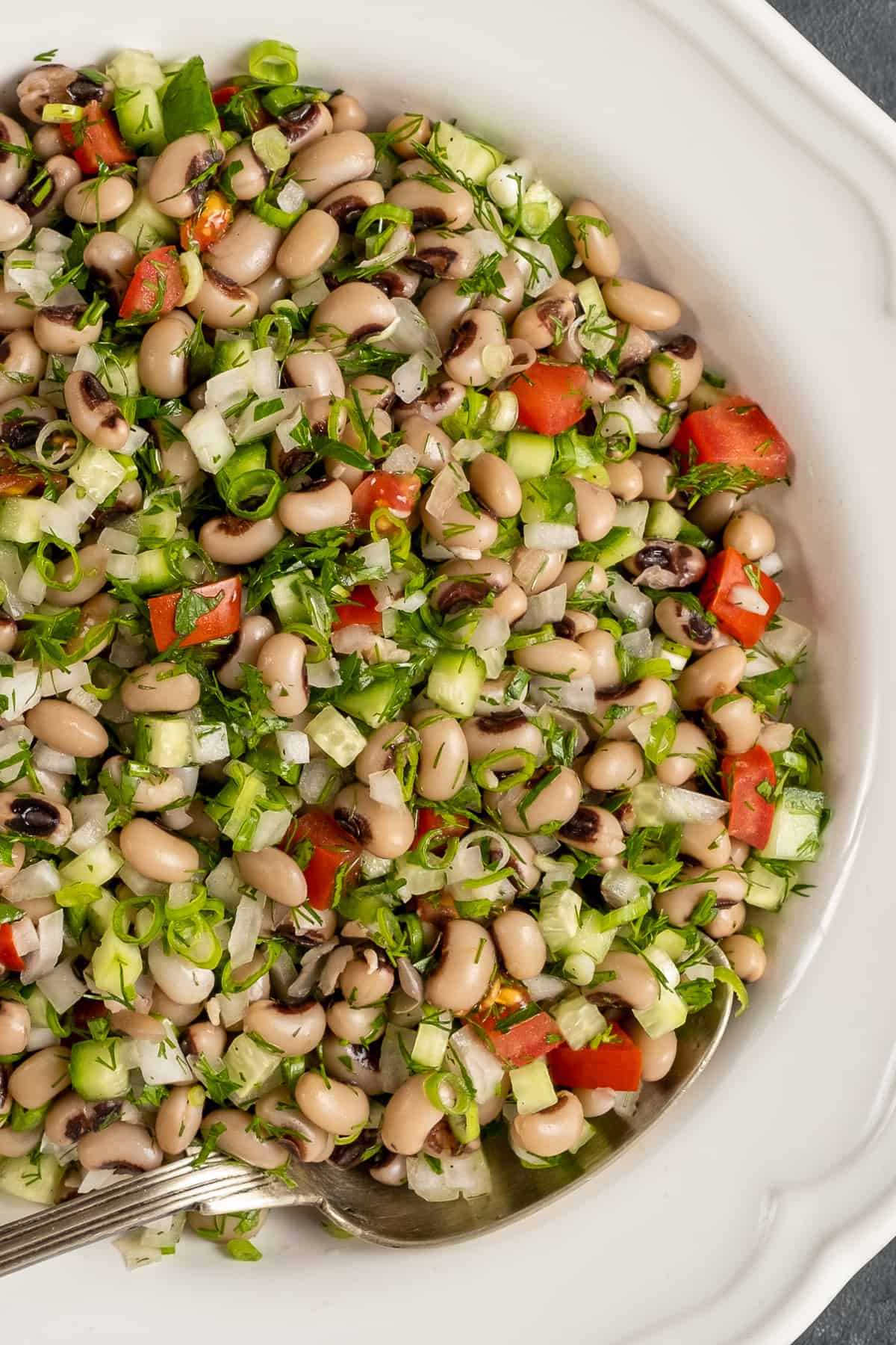 Black eyed pea salad in a white bowl and a spoon in it.