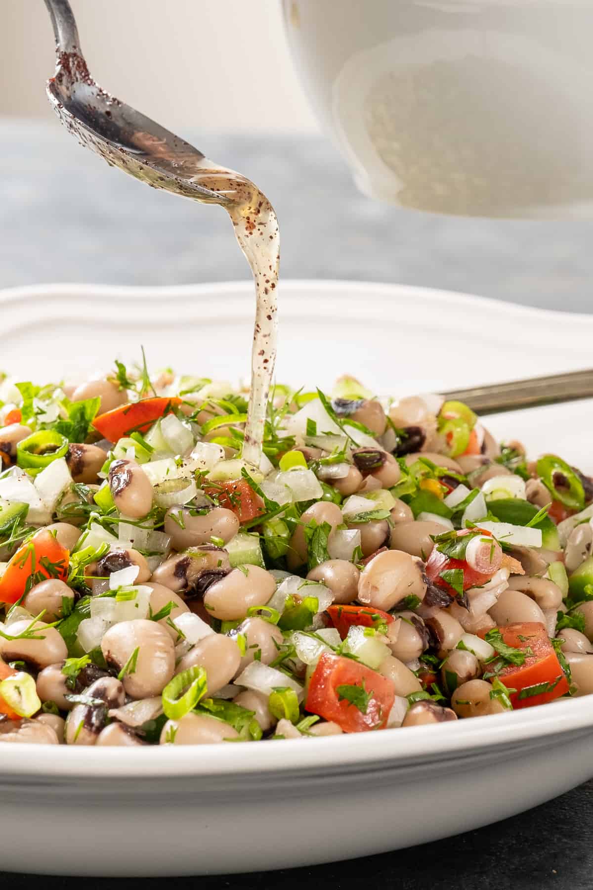 A spoon drizzling lemon dressing over bean salad.