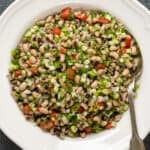 Black eyed pea salad with vegetables and herbs in a white bowl and a spoon in it.