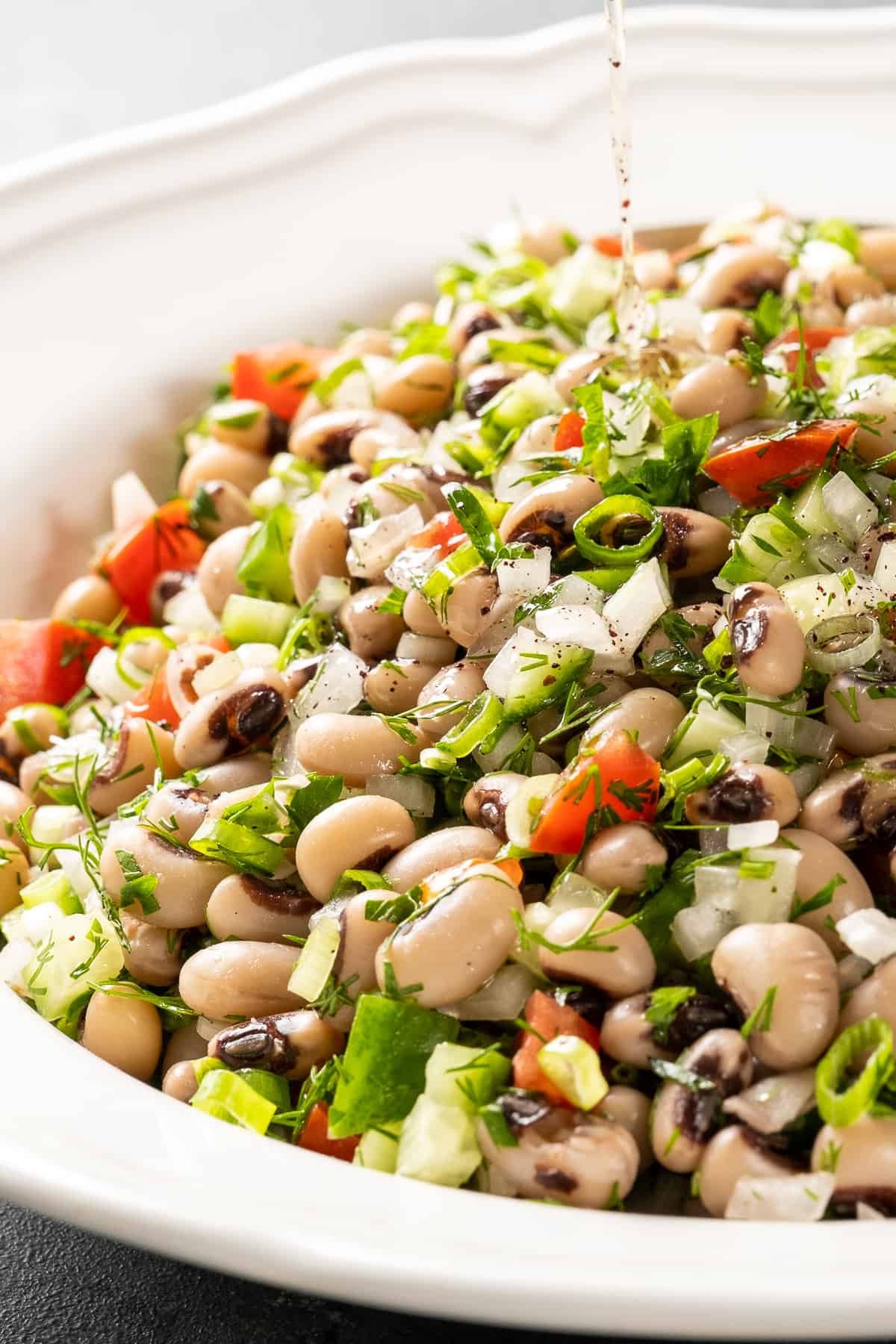 Black eyed beans salad with herbs, cucumber and tomatoes in a white bowl.