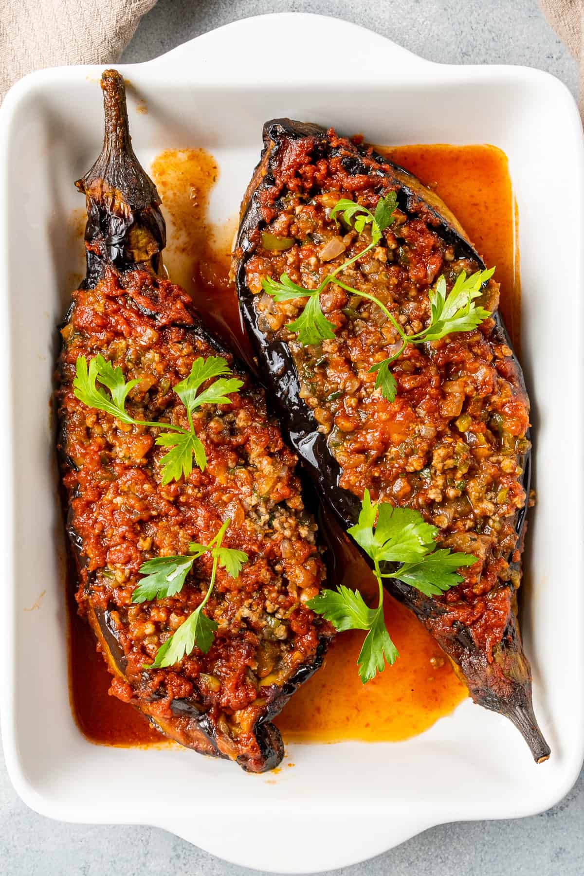 Turkish karnıyarık made with roasted eggplants stuffed with seasoned ground beef and baked in tomato sauce, garnished with fresh parsley.
