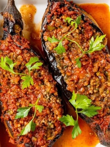 Turkish karnıyarık made with roasted eggplants stuffed with seasoned ground beef and baked in tomato sauce, garnished with fresh parsley.