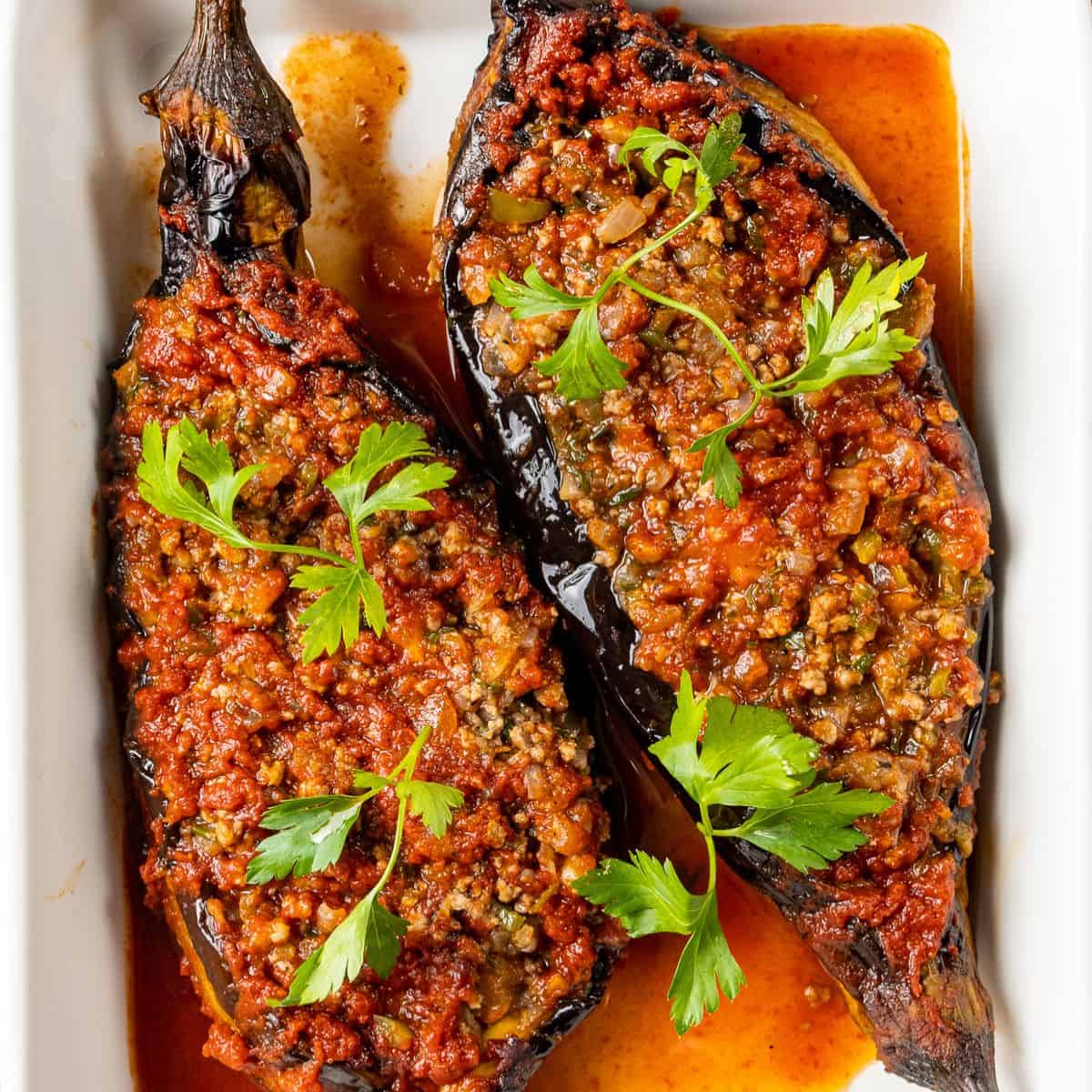 Turkish karnıyarık made with roasted eggplants stuffed with seasoned ground beef and baked in tomato sauce, garnished with fresh parsley.
