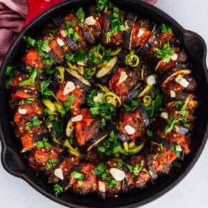 An image of baked eggplant kebab in a pan, topped with garlic, peppers, and fresh parsley.
