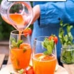 Refreshing strawberry mint lemonade being poured into glasses, garnished with fresh mint and strawberries.