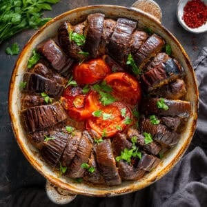 Turkish eggplant kebab baked with meatballs, tomatoes and garlic in a round baking dish, garnished with chopped parsley.