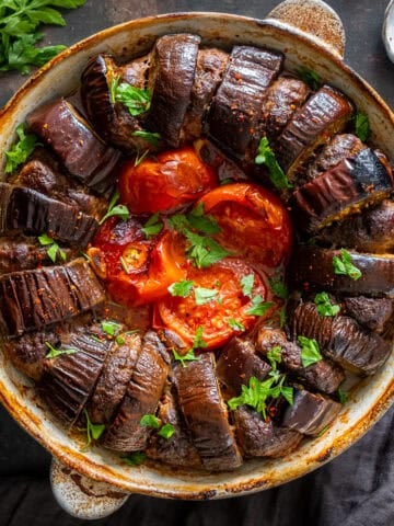 Turkish eggplant kebab baked with meatballs, tomatoes and garlic in a round baking dish, garnished with chopped parsley.
