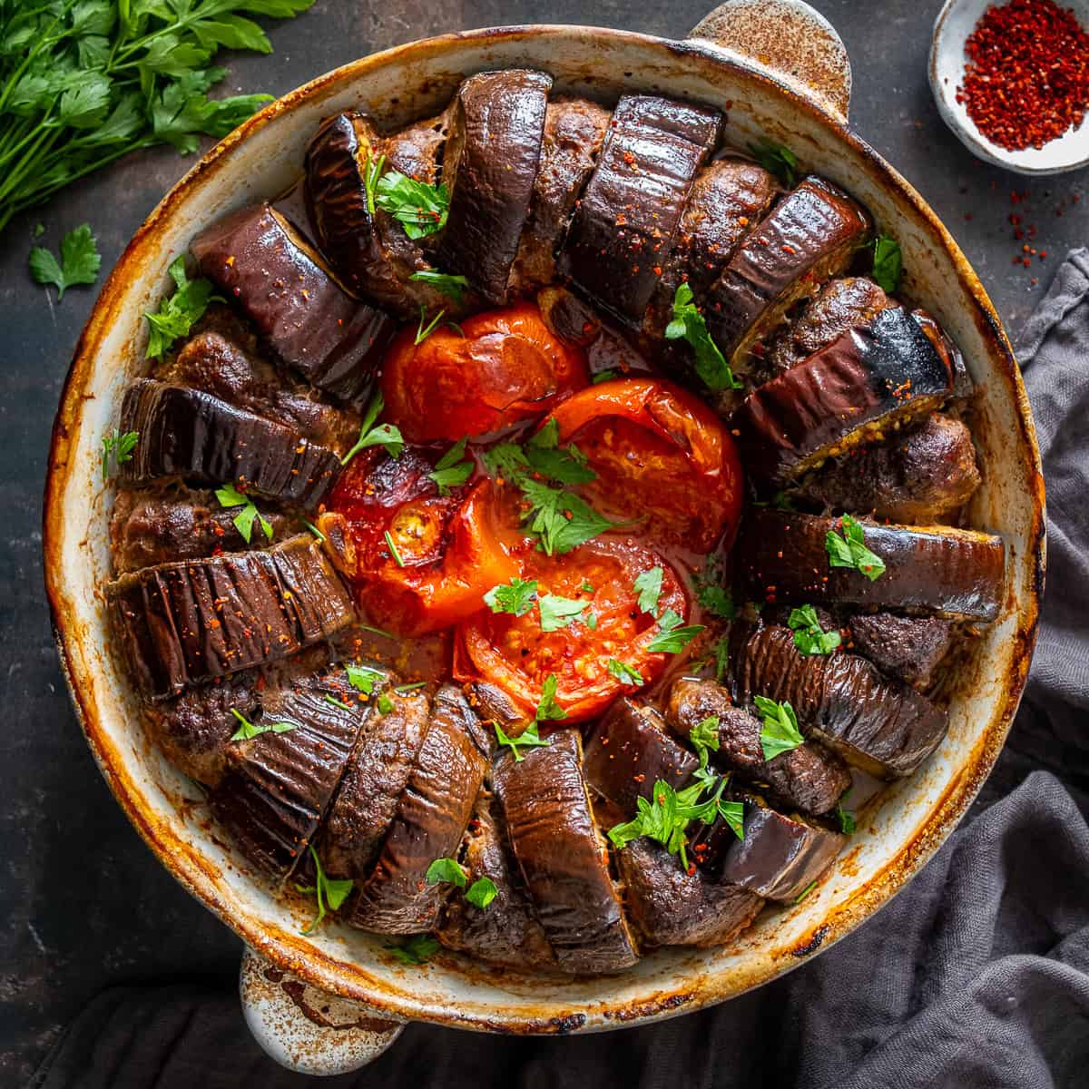 Turkish eggplant kebab baked with meatballs, tomatoes and garlic in a round baking dish, garnished with chopped parsley.