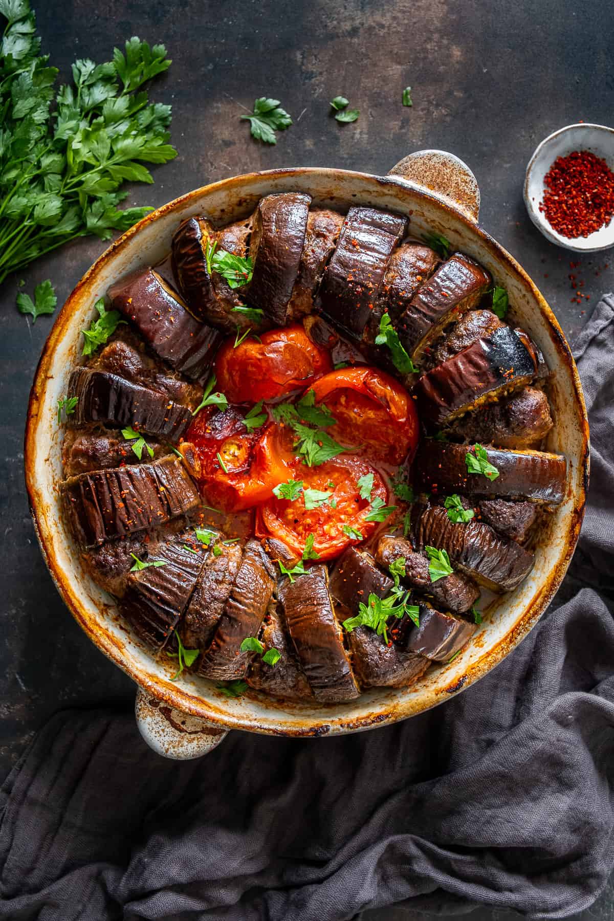 Baked Turkish eggplant kebab with meatballs, tomatoes and garlic in a round baking dish, garnished with chopped parsley.