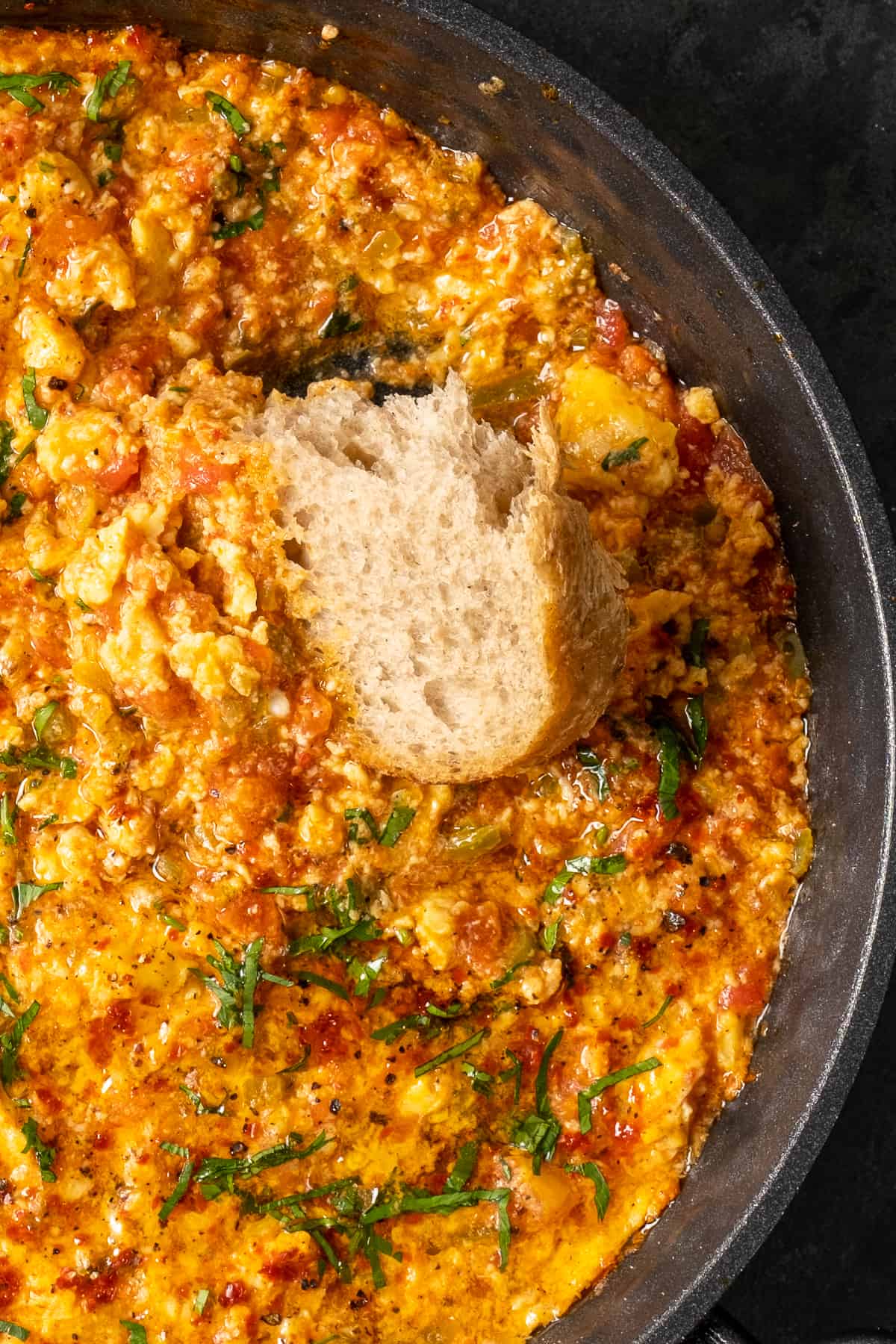 A piece of bread dipped into menemen in a pan.