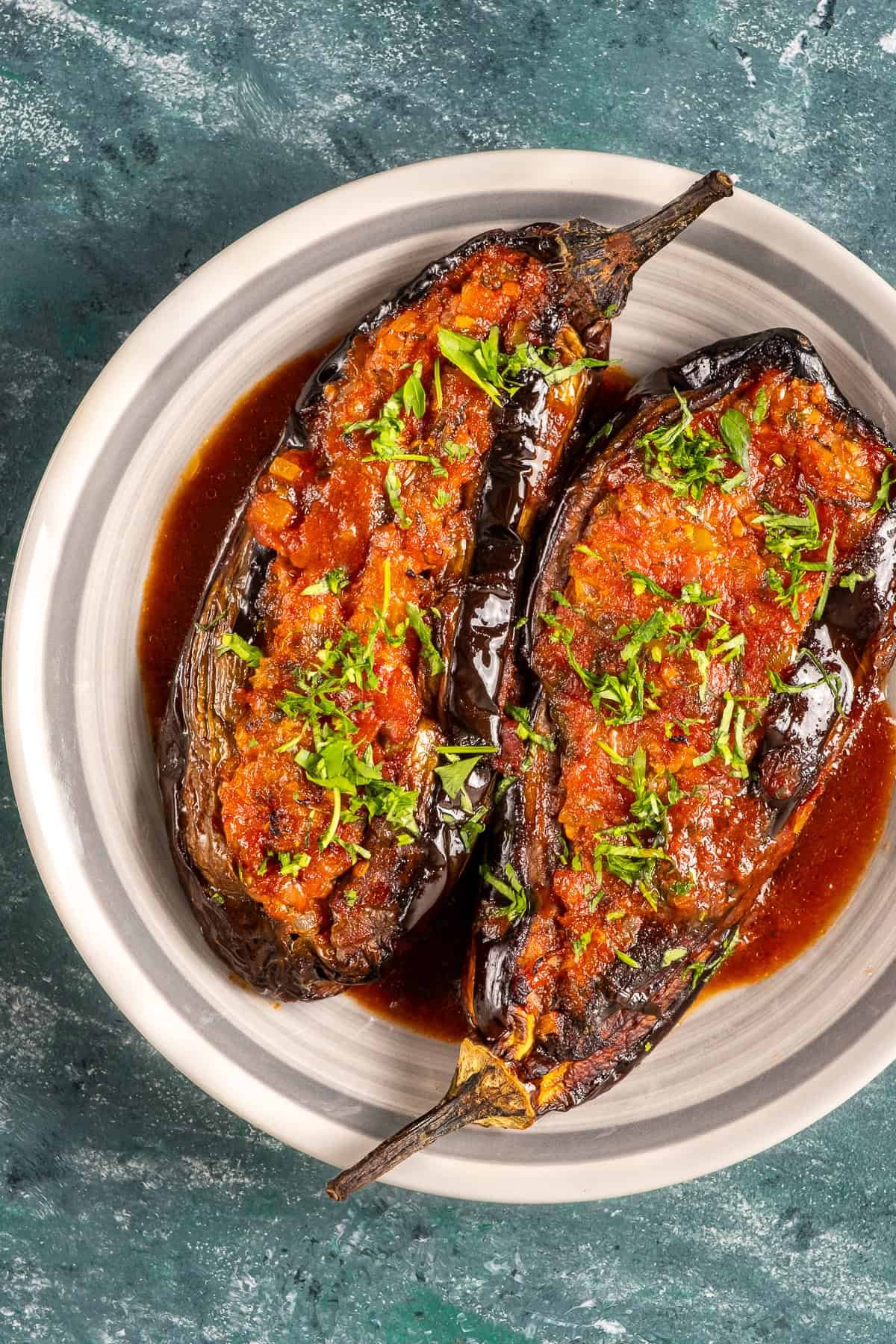 Two Turkish stuffed eggplants with tomato-onion filling, garnished with fresh herbs and served in a rich olive oil sauce.
