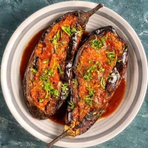 Two Turkish stuffed eggplants with tomato-onion filling, garnished with fresh herbs and served in a rich olive oil sauce.