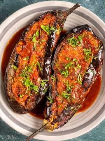Two Turkish stuffed eggplants with tomato-onion filling, garnished with fresh herbs and served in a rich olive oil sauce.