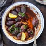 A dish of Sogan Dolmasi (Turkish Stuffed Onions) served in a rustic white enamel pan, garnished with fresh parsley and lemon wedges.