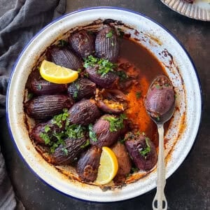 A dish of Sogan Dolmasi (Turkish Stuffed Onions) served in a rustic white enamel pan, garnished with fresh parsley and lemon wedges.
