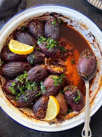 A dish of Sogan Dolmasi (Turkish Stuffed Onions) served in a rustic white enamel pan, garnished with fresh parsley and lemon wedges.