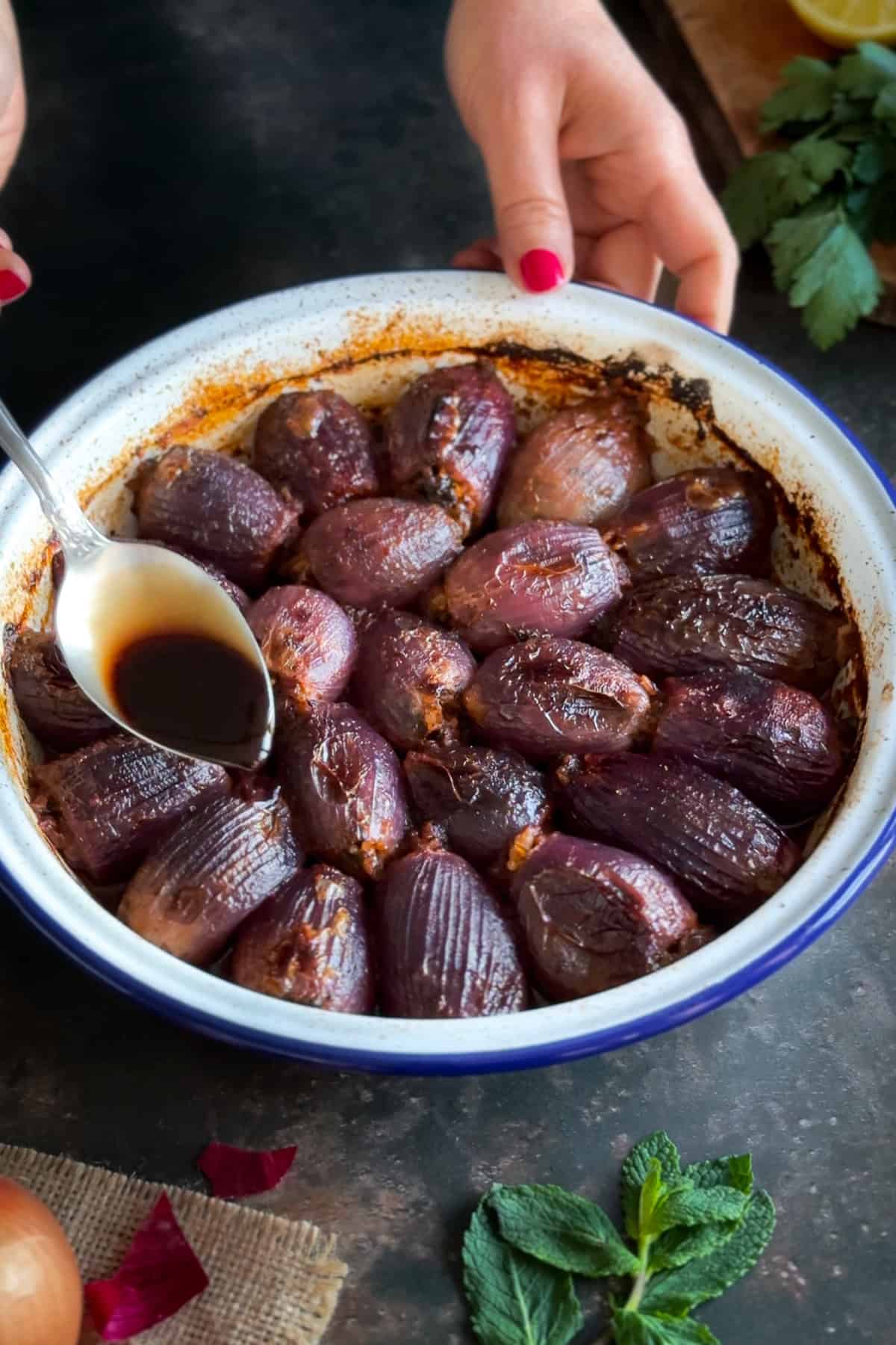 A dish of Sogan Dolmasi (Turkish Stuffed Onions) fresh out of the oven, with a spoon drizzling pomegranate molasses over the top.