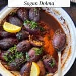 Turkish stuffed onions (Sogan Dolma) in tomato sauce, garnished with parsley and lemon wedges, in a serving dish with a spoon.