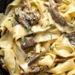 Oyster mushroom pasta made with pappardelle in a creamy sauce, topped with sautéed oyster mushrooms and chopped herbs, served in a dark bowl.