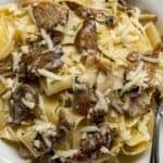 Oyster mushroom pasta made with pappardelle in a creamy sauce, topped with sautéed oyster mushrooms and grated cheese, served in a white bowl with a fork on the side.