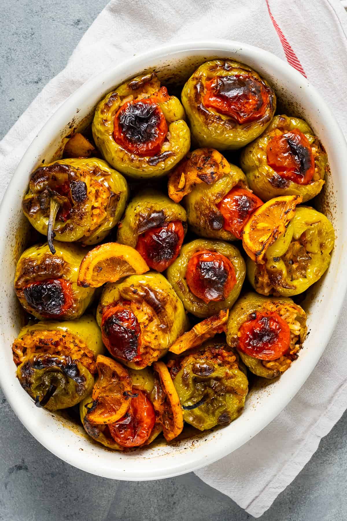 Baked Turkish stuffed peppers with golden tops, cherry tomatoes, and lemon slices in a white dish.