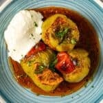 Turkish stuffed peppers (biber dolması) served with yogurt on a blue plate, in a rich tomato-based sauce with roasted tomatoes and herbs.