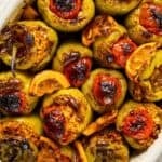 Tray of Turkish stuffed peppers (biber dolması) filled with rice, topped with roasted tomatoes and lemon slices, baked until lightly charred.