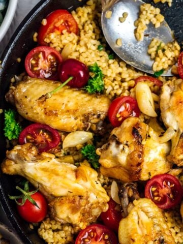 Chicken wings in a cast iron pan with bulgur wheat and garnished with cherry tomatoes and parsley.