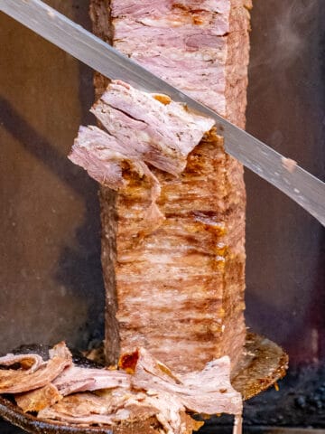 Turkish doner is being sliced thinly with a large knife into a wooden spoon.