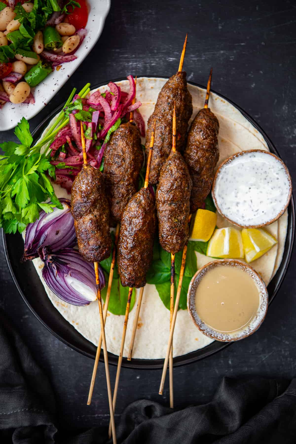 Kofta kebabs served with flat bread, parsley, onions and sauces on a plate.