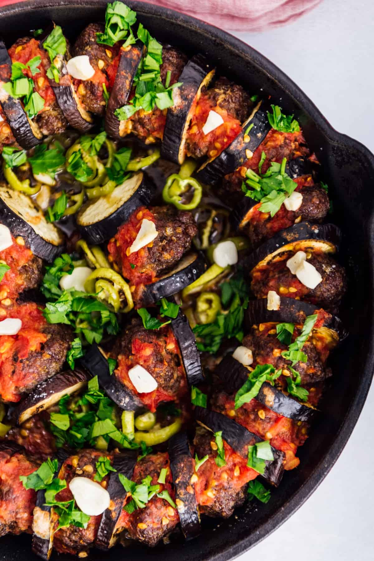 Baked eggplant slices and meatballs in a cast iron pan garnished with a tomato sauce and chopped parsley.