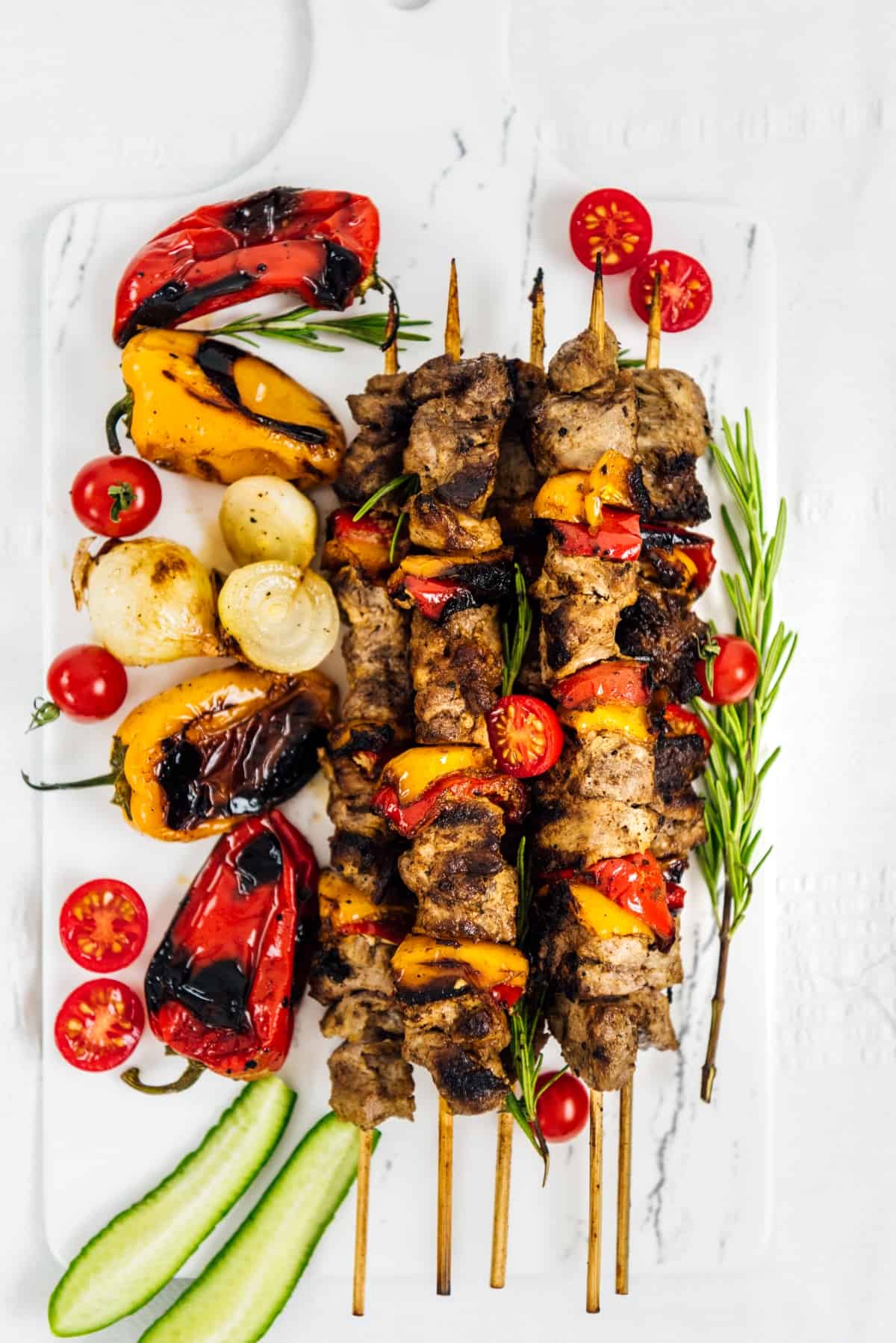 Shish kebabs served with roasted veggies on a white serving board.