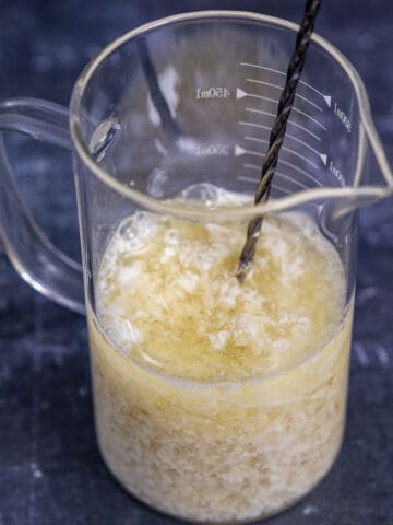 Almond milk and vinegar mixture in a glass measuring cup and a stirring spoon inside it.