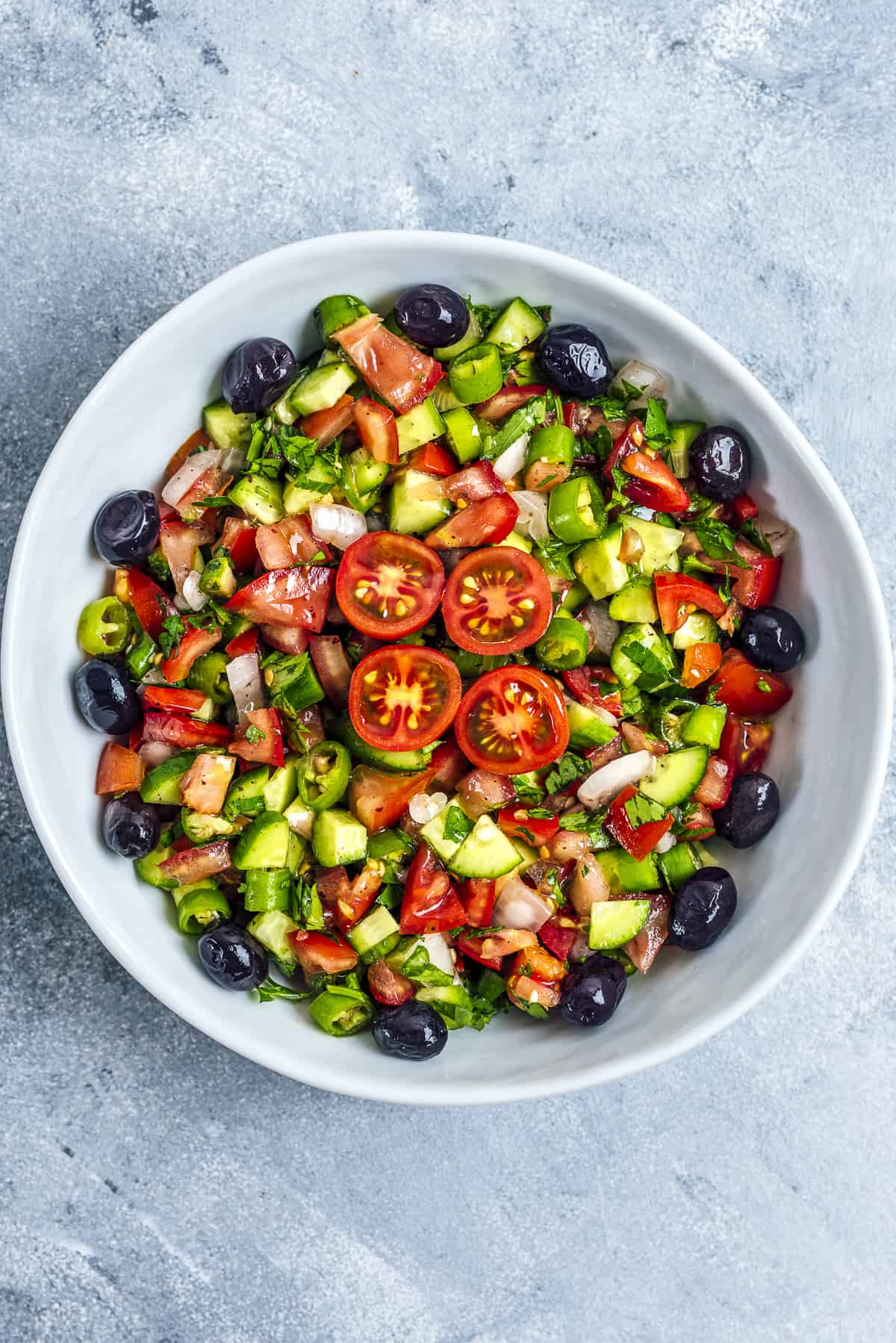 Tomato and cucumber salad garnished with black olives in a white bowl.